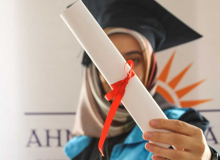 Mulher em beca de formatura segurando diploma, celebrando conquista acadêmica