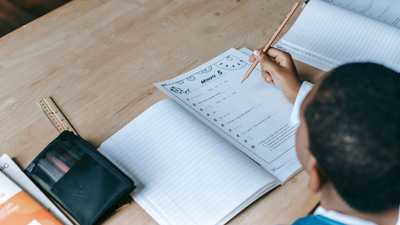 Estudante escrevendo em caderno durante atividade escolar