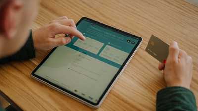 Pessoa realizando pagamento online com tablet e cartão de crédito sobre mesa de madeira