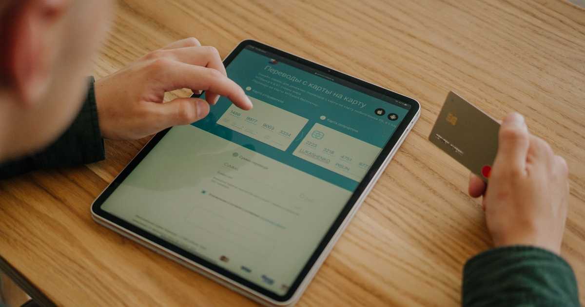 Pessoa realizando pagamento online com tablet e cartão de crédito sobre mesa de madeira