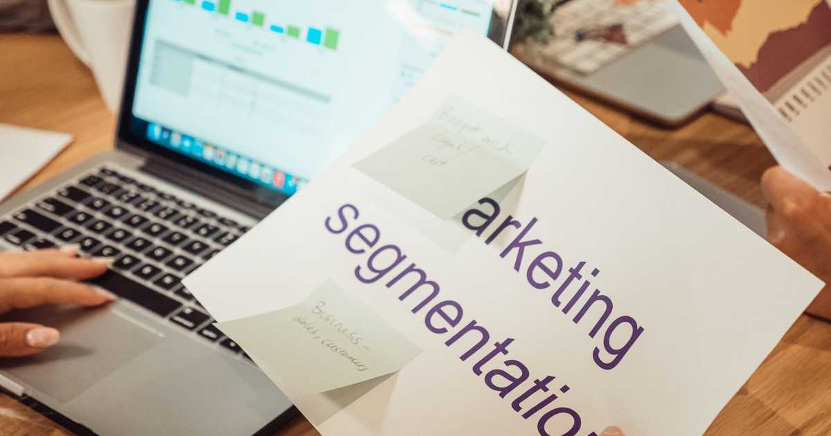 Mãos analisando dados de marketing em laptop e documentos de papel