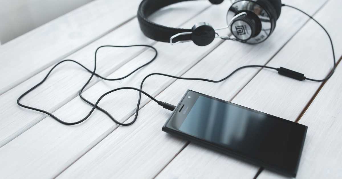 Smartphone conectado a fones de ouvido sobre uma mesa de madeira