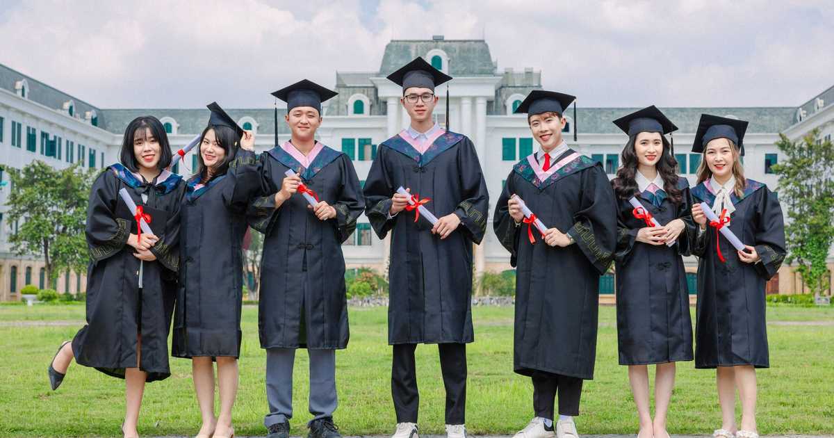 Grupo de formandos em toga segurando diplomas em frente a prédio universitário