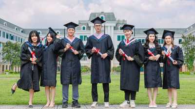 Grupo de formandos em toga segurando diplomas em frente a prédio universitário
