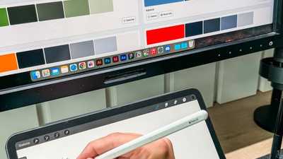 Designer usando caneta digital em tablet com paleta de cores exibida em monitor