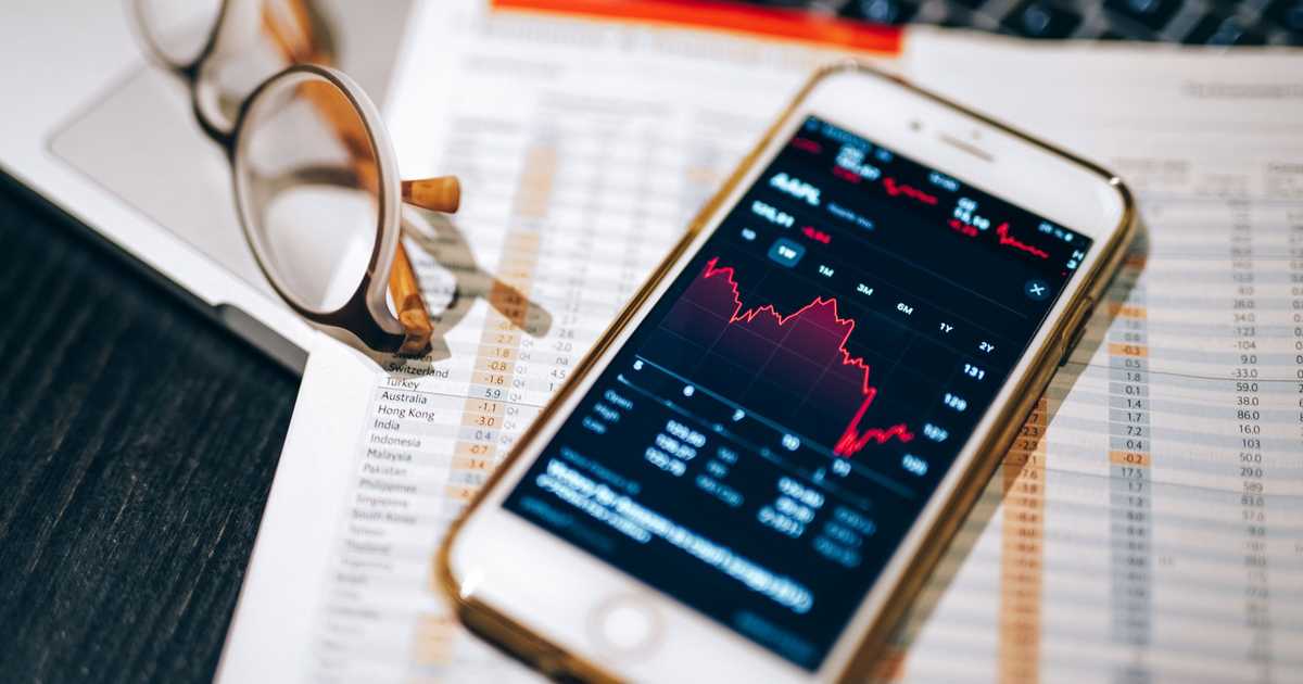 Smartphone exibindo gráfico do mercado de ações sobre planilha financeira