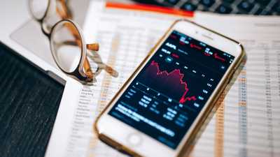 Smartphone exibindo gráfico do mercado de ações sobre planilha financeira