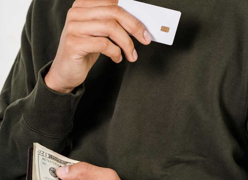 Homem segurando cartão de crédito e dinheiro, avaliando opções de pagamento