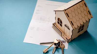 Miniatura de casa de madeira com chaves e contrato, simbolizando transação imobiliária