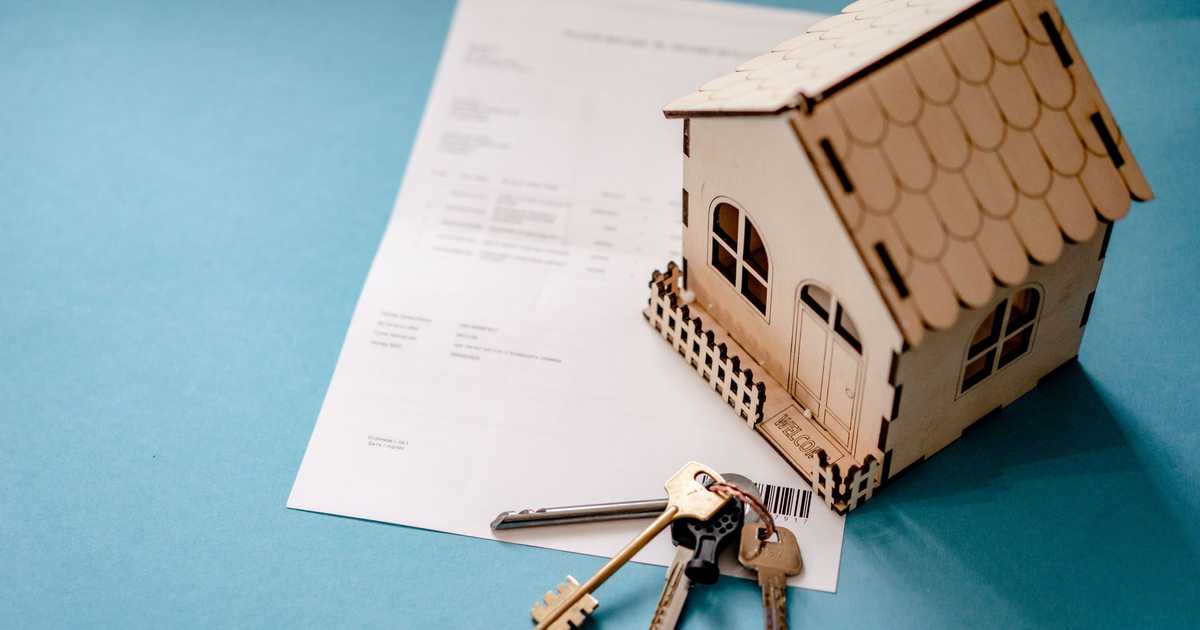 Miniatura de casa de madeira com chaves e contrato, simbolizando transação imobiliária